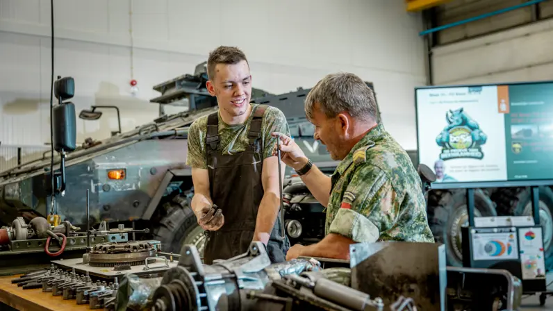 een monteur die aan een collega uitleg geeft over een voertuigmotor. 