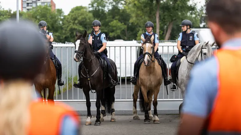 De combinaties staan opgesteld naast elkaar, buiten. Vlak voor de camera staan figuranten.