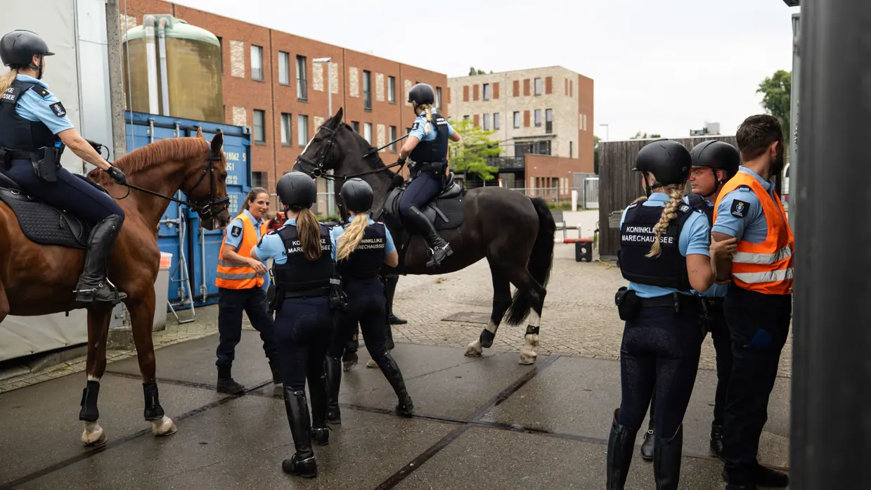 Tumult rondom de paarden. Twee ruiters begeleiden het geheel. Een figurant met een oranje hesje wordt geboeid. 