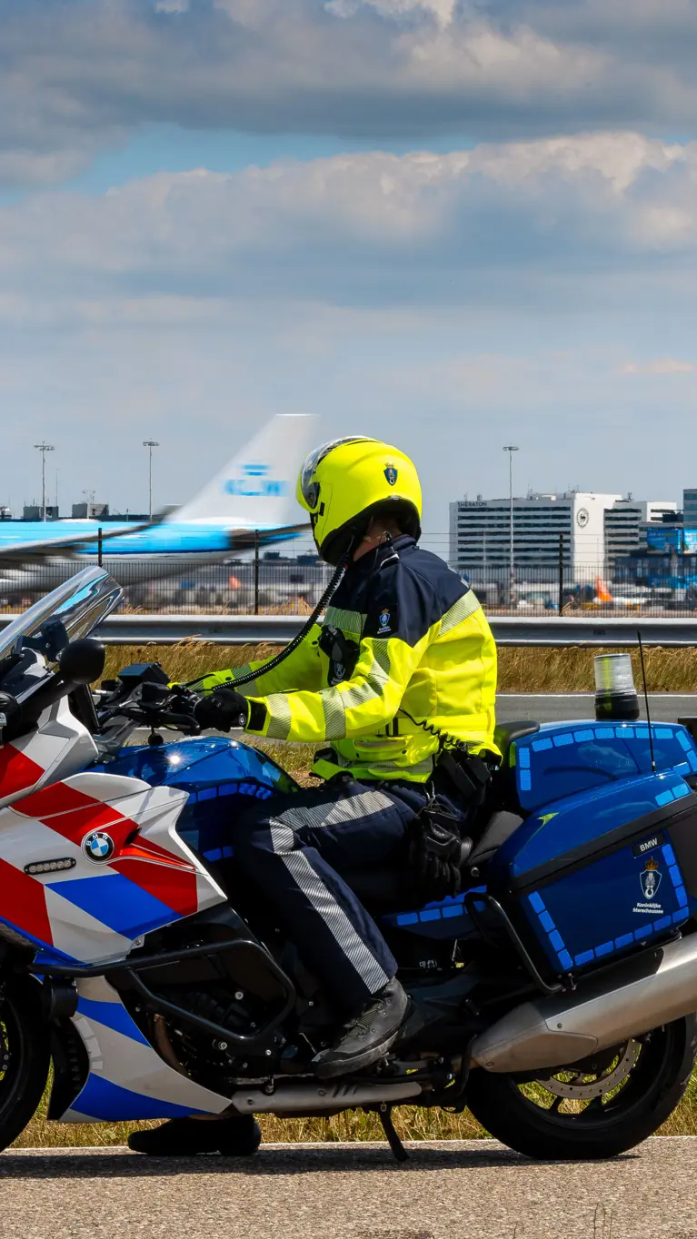 Motorrijder van de Marechaussee, op de rug gezien met Schiphol op de achtergrond