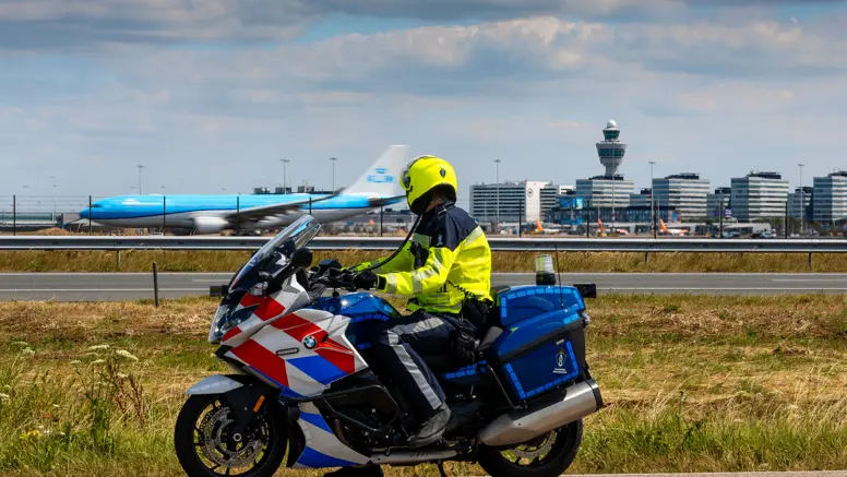 Motorrijder van de Marechaussee, op de rug gezien met Schiphol op de achtergrond