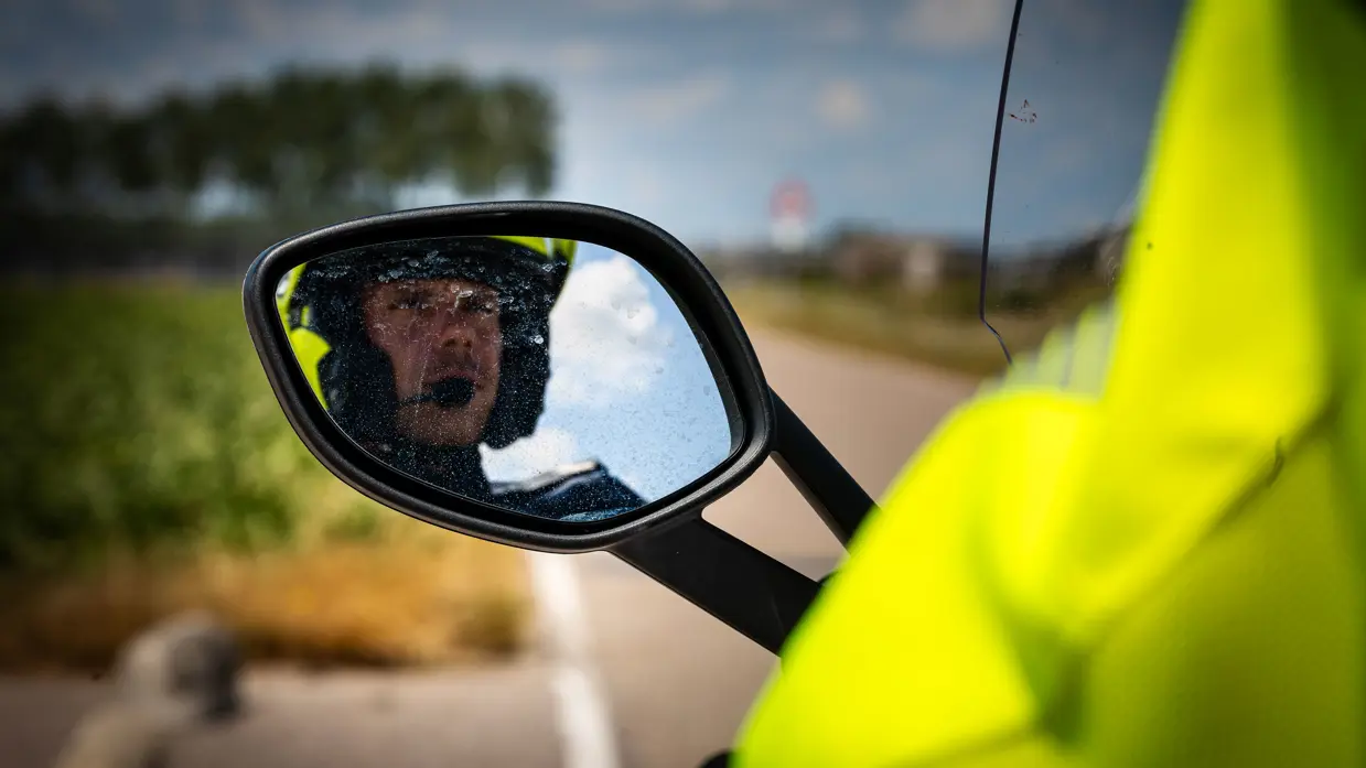 Wachtmeester van de Marechaussee kijkt in de zijspiegel van zijn motor.