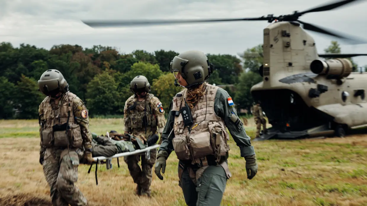 Drie militairen vervoeren een collega op een brancard van een helikopter weg.