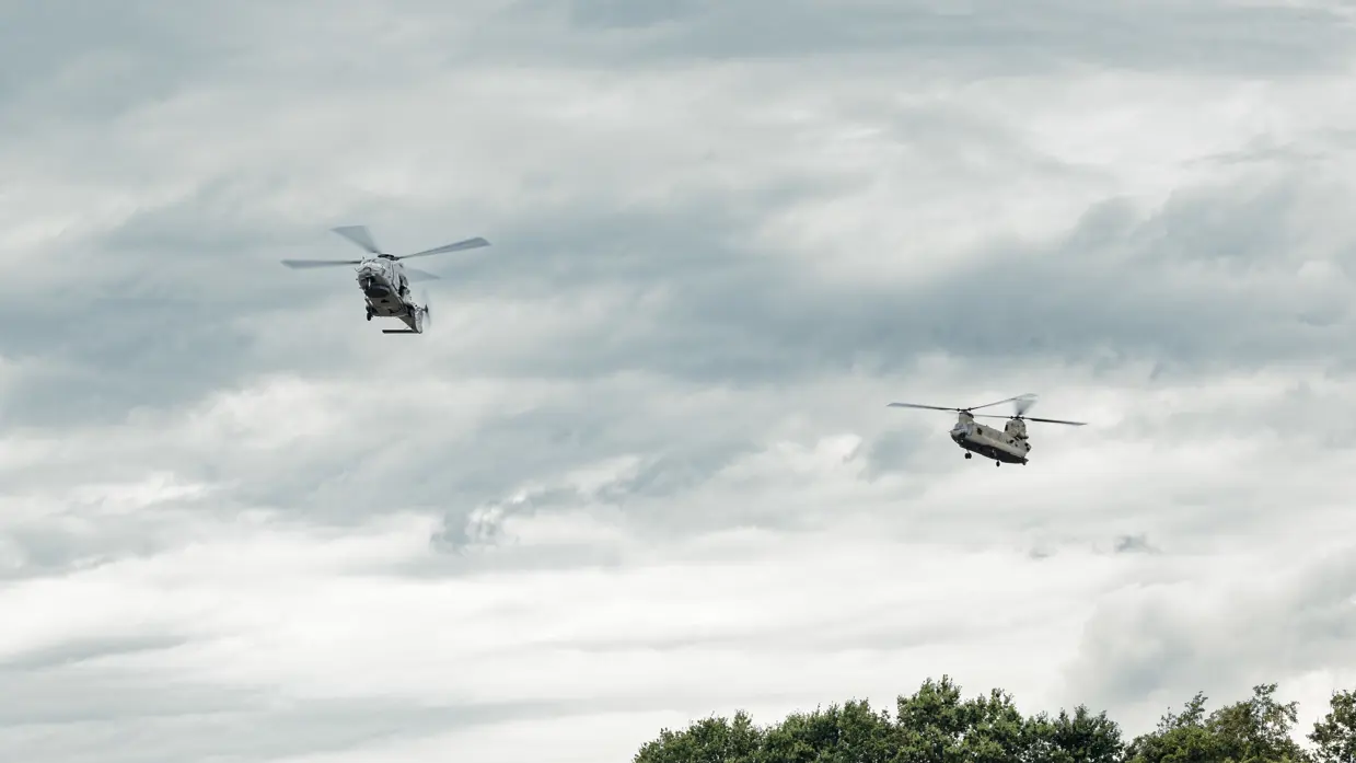 Twee helikopters vliegen hoog in de lucht.