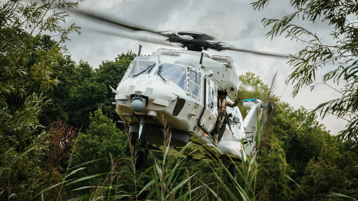 Een witte helikopter vliegt tussen bomen.
