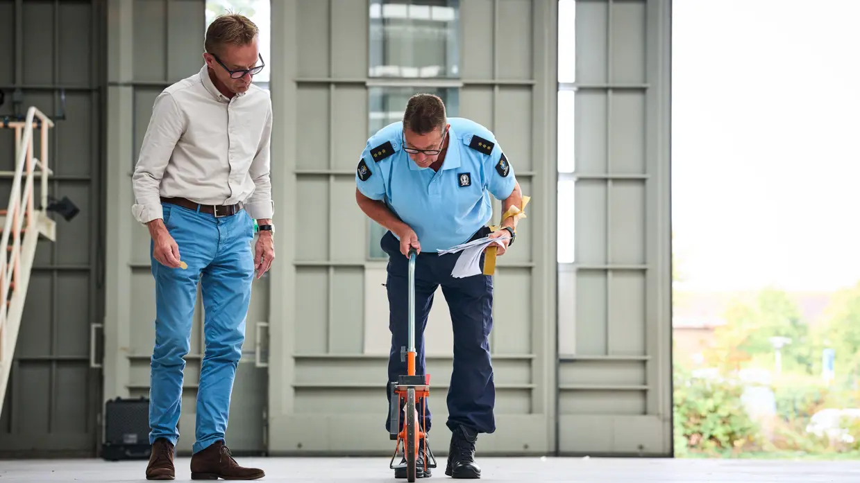 Met een rolmeter meet Dennis de afstand op de vloer van de hal.