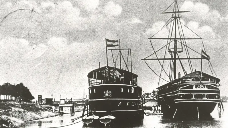 2 historische schepen, een stoomschip en een zeilschip, afgemeerd in een haven bij Gorinchem, met vlaggen en mensen aan boord.
