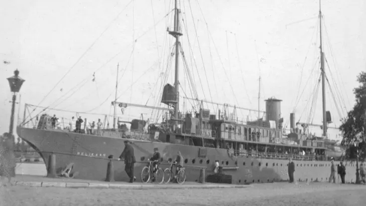 Een groot oud schip genaamd Pelikaan ligt aan de kade, met mensen en fietsen op de voorgrond.