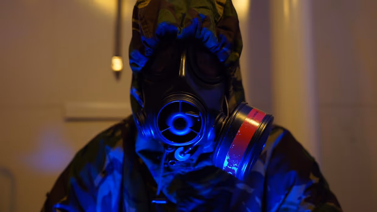 Een bemanningslid draagt een gasmasker en een beschermend pak.