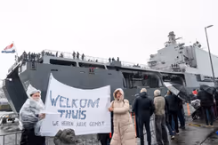 Mensen in regenkleding met spandoek Welkom Thuis bij aankomst marineschip.