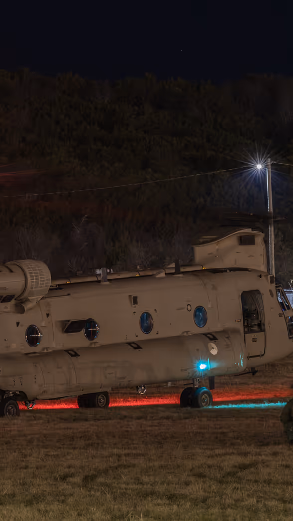Nachtopname van een Chinook op de grond met luchtmobiele infanteristen er omheen.