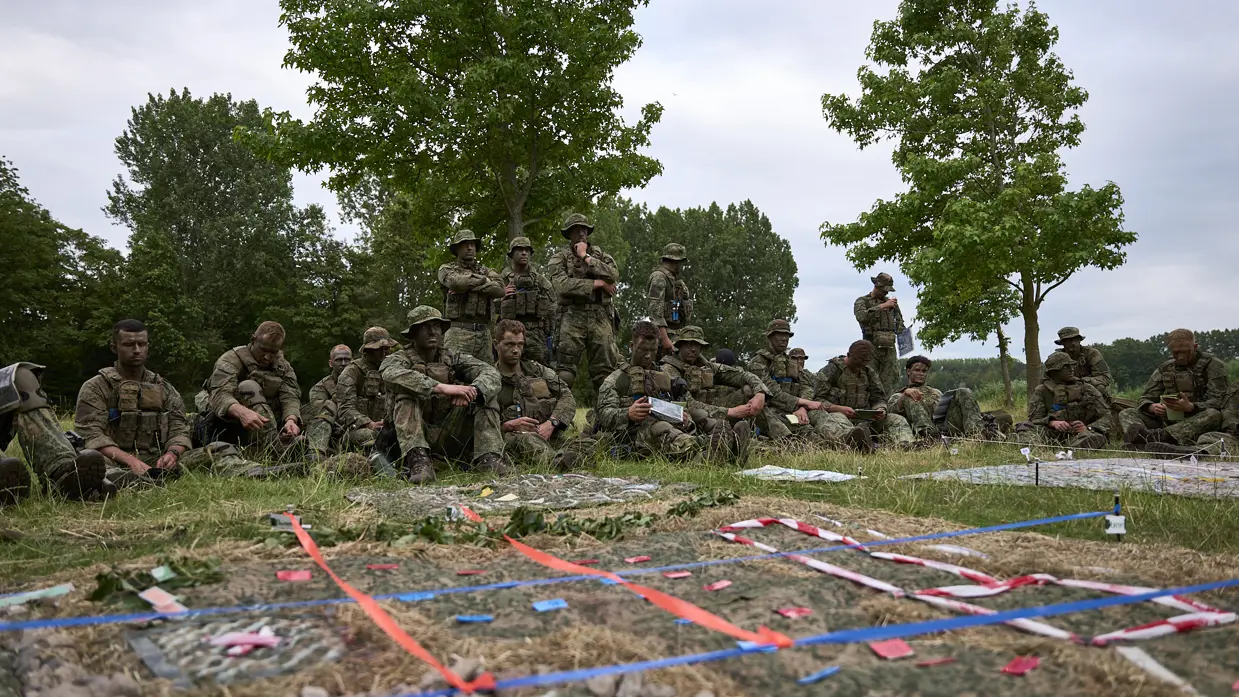 Mariniers zitten in het gras en bekijken een geïmproviseerde maquette.