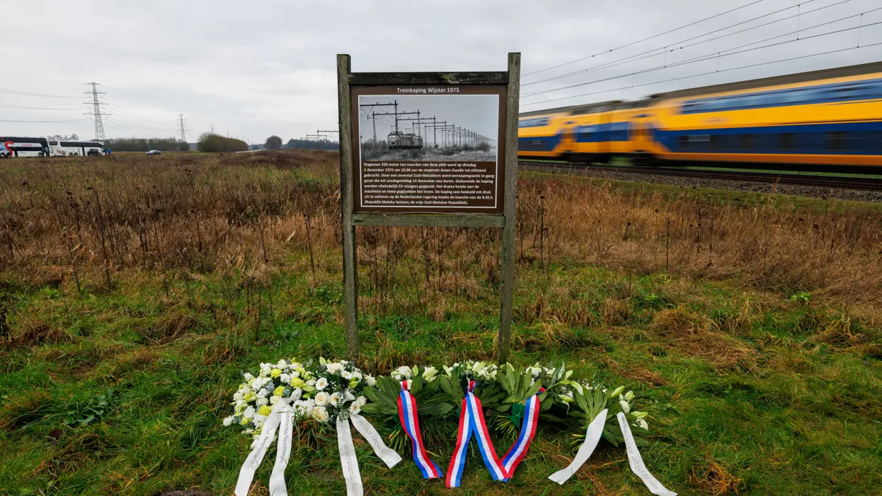 Links een groep mensen, waaronder militairen in uniform bij een bord langs de spoorlijn. Rechts: bloemen en kransen bij een bord met daarop een afbeelding van een oude trein, terwijl een moderne trein langs raast.