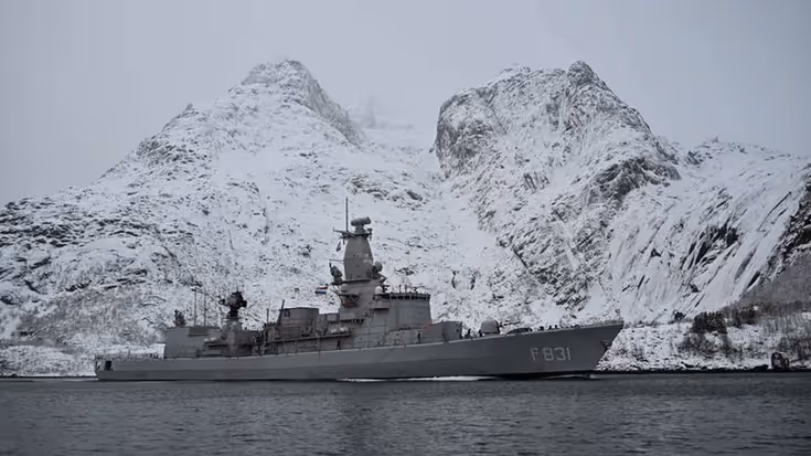 De Zr.Ms. Van Amstel vaart voor besneeuwde rotsen langs.
