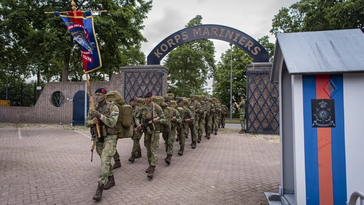 De geslaagden lopen achter hun vaandel de oude poort binnen van de Van Ghentkazerne. Rechts een wachthuisje.