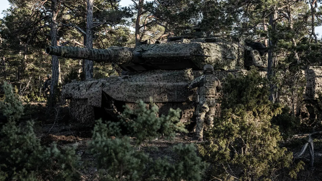 Militairen en hun voertuigen, gecamoufleerd in het bos.