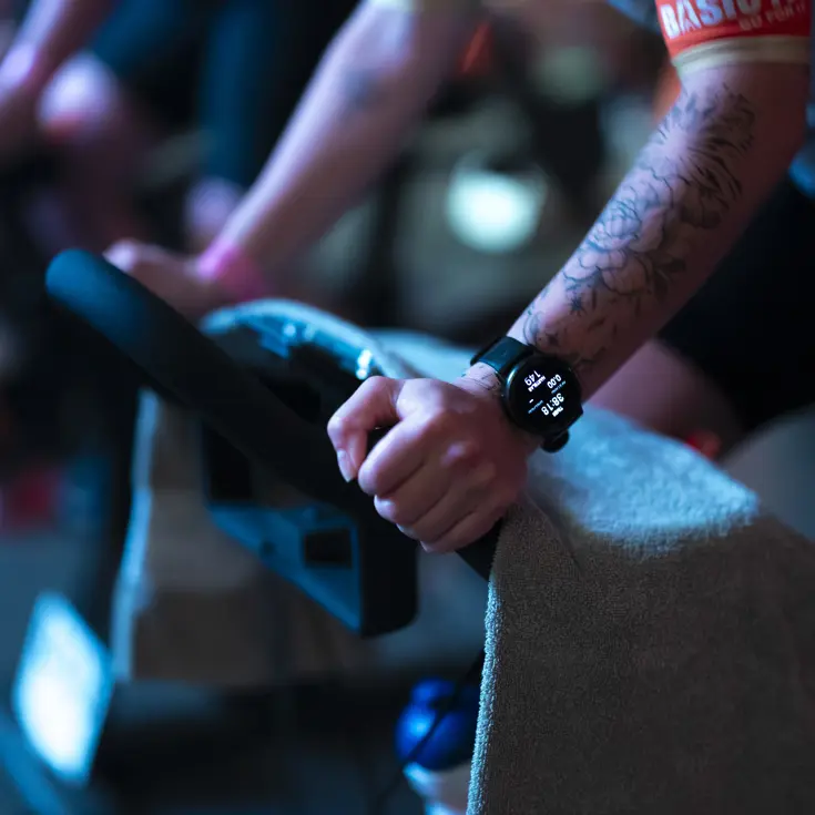 Close up van sporthorloge en handen op het stuur van een indoorbike.