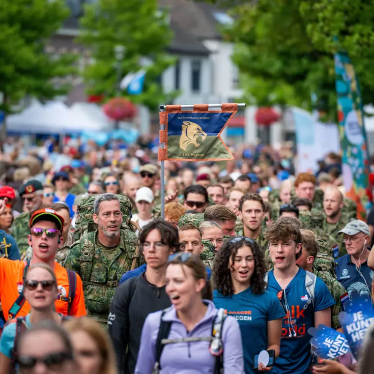 Een groep mensen aan de wandel tijdens de 4Daagse, in het midden een club militairen van 103 Marechaussee Eskadron.