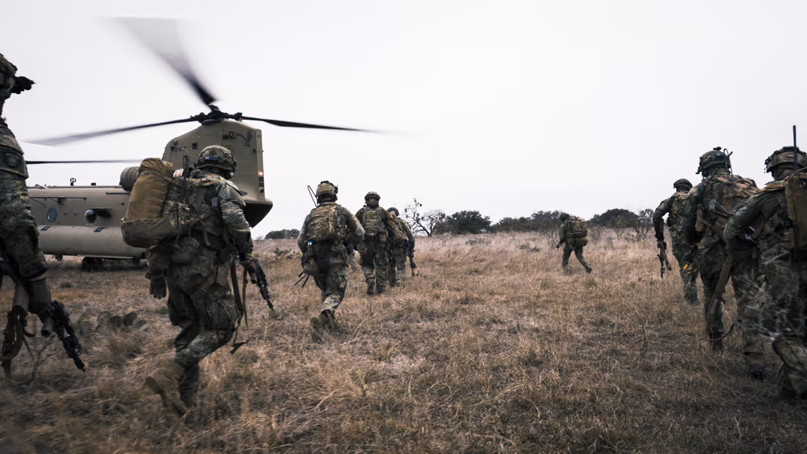 In het veld lopen landmachtmilitairen naar de openstaande achterklep van een Chinook met draaiende rotorbladen.