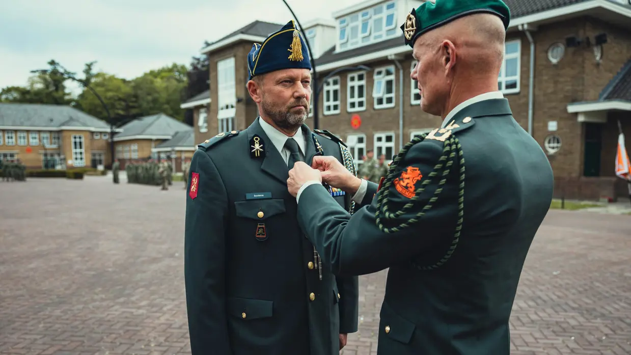 Generaal Swillens bevestigt een koord of iets dergelijks aan het DT-jasje van de adjudant Klaas Bootsma. 