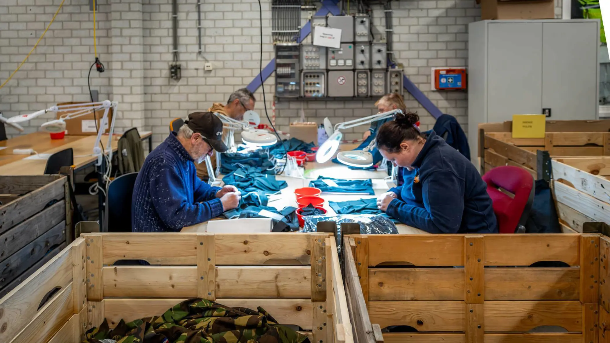 4 personen, van wie een met pet, werken met kleding aan een tafel.  