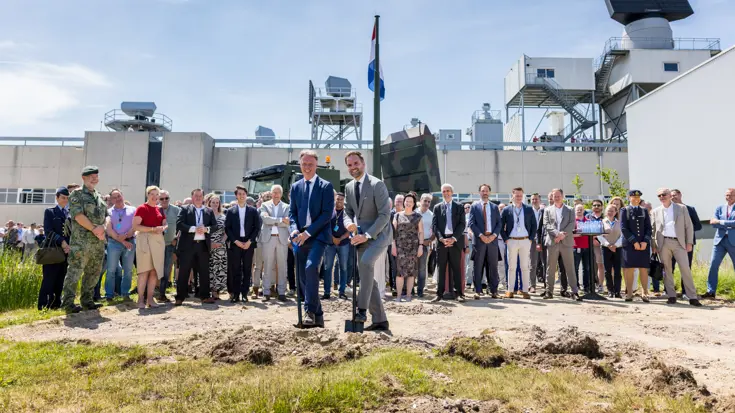 Een aantal burgers en militairen. Twee mensen steken een schop in de grond.