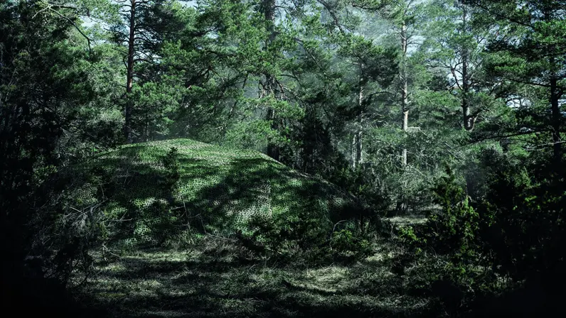Een militair voertuig in het bos verstopt onder een groot camouflagenet.