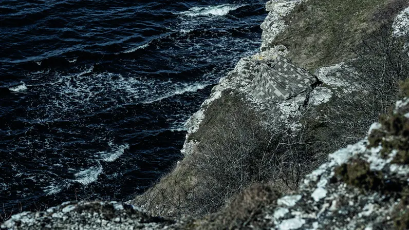 Enkele militairen verstopt op een berg aan zee onder een camouflagedeken.