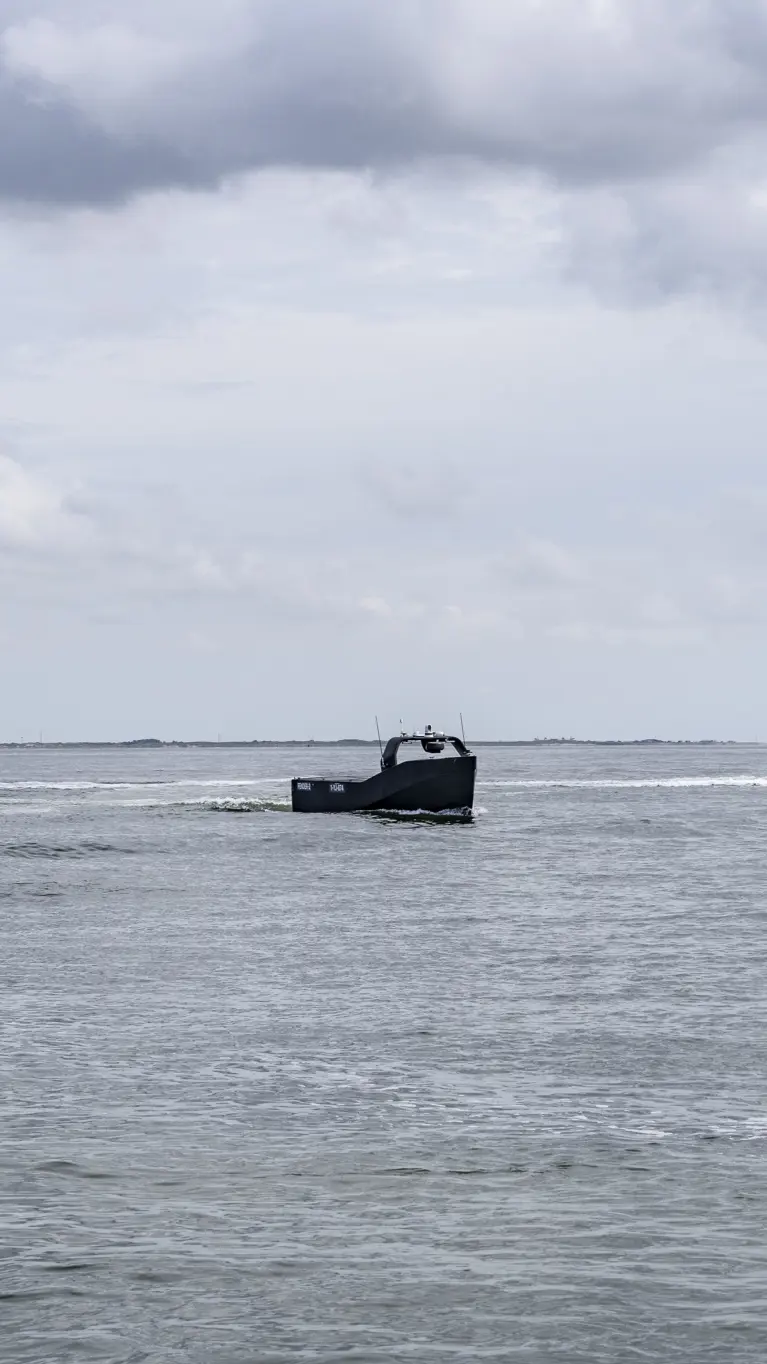 Klein onbemand bootje vaart tussen 2 grote schepen op zee.