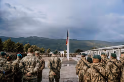 Infanteristen op  de rug gezien met een vlag op de achtergrond en daarachter heuvels.