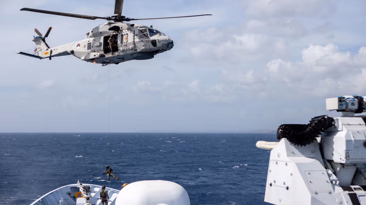 Militair daalt met touw uit helikopter op dek van schip.