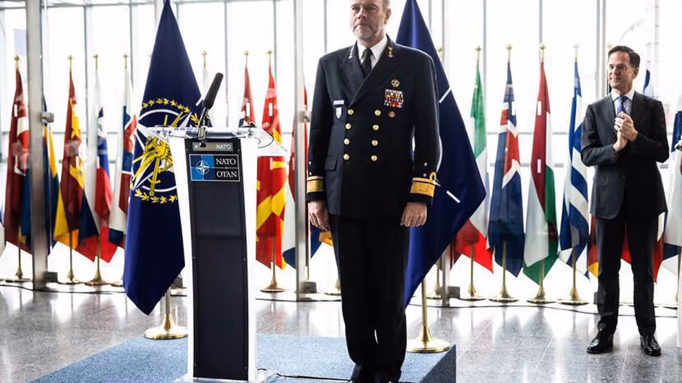 Rob Bauer in de houding naast een katheder met NAVO-logo erop. Op de achtergrond secretaris-generaal Mark Rutte.