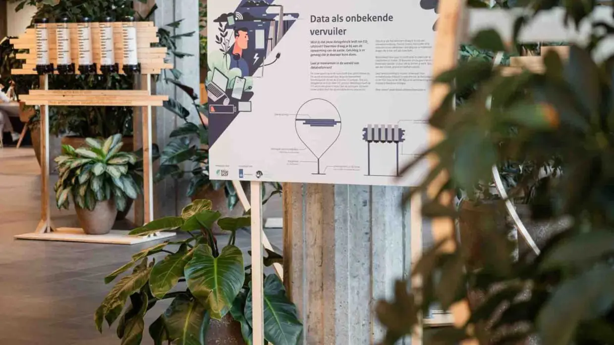  links: 2 informatieborden tussen plantenbakken in een hal. Rechts: Een houten onderzetter met stalen tafelpoot.