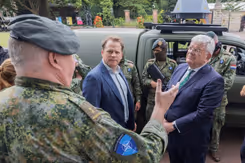 Gijs Tuinman en burgemeester Jan van Zaanen praten buiten met militair. Op de achtergrond voertuig en militairen.