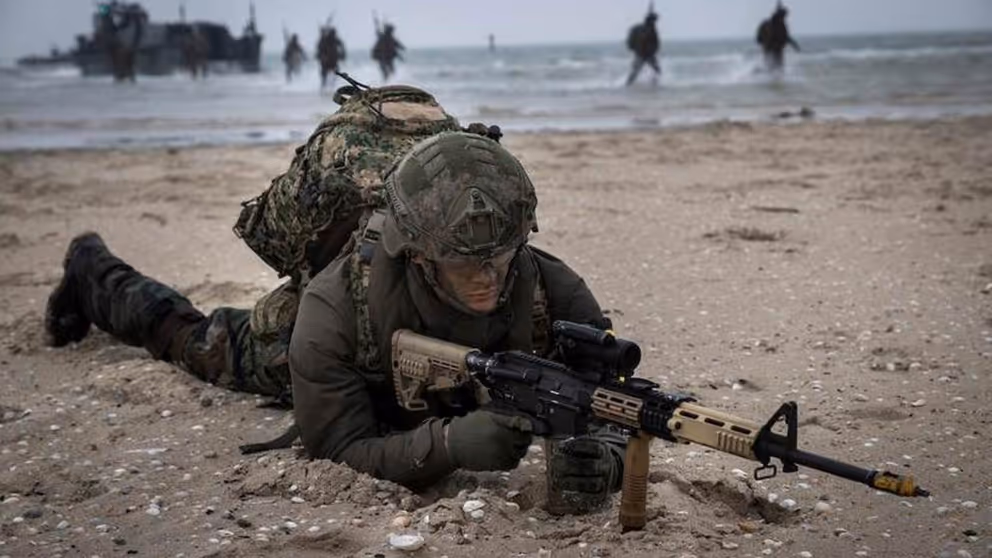 Militair ligt tijdens oefening met wapen gericht op zijn buik op een strand.