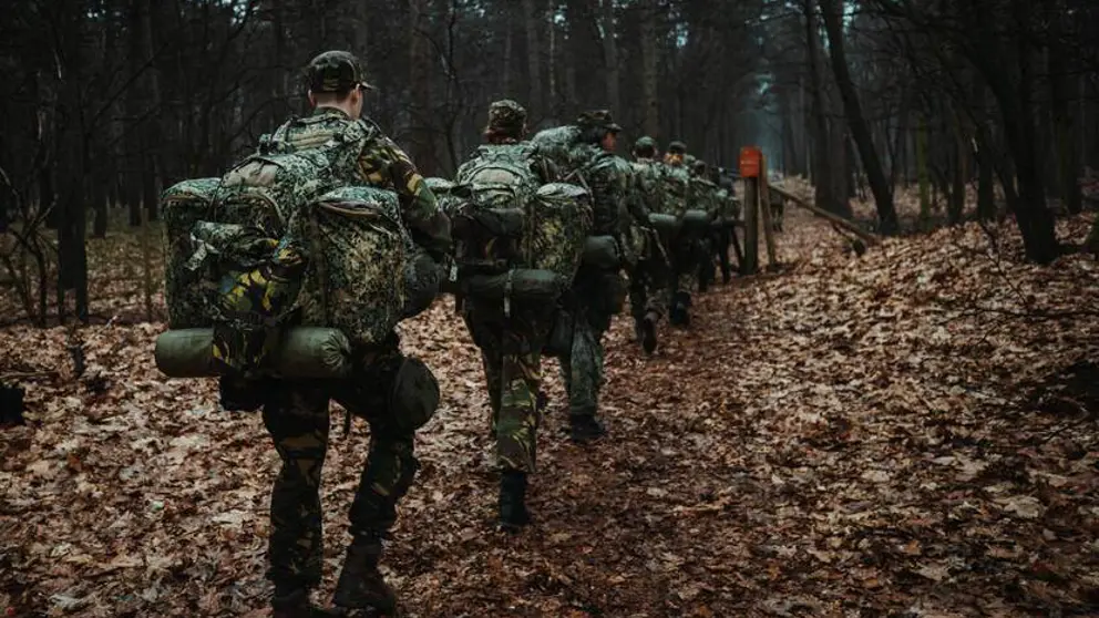 Reservisten lopen met bepakking door een bos.
