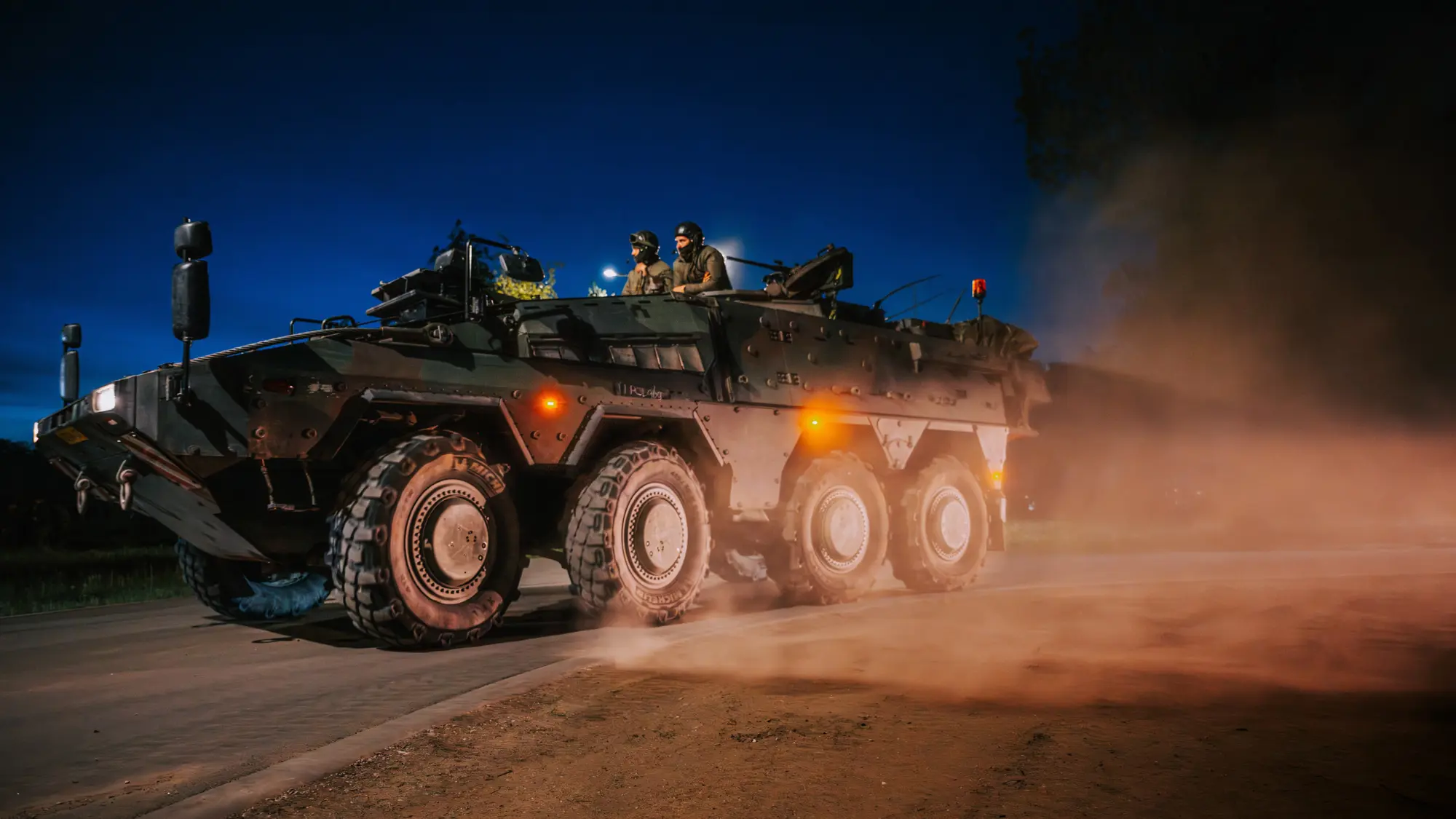 Militairen rijden in pantservoertuig over stoffige weg bij duisternis.