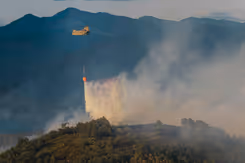 Chinook-helikopter die water uit een oranje bambi bucket laat vallen op brandend terrein.