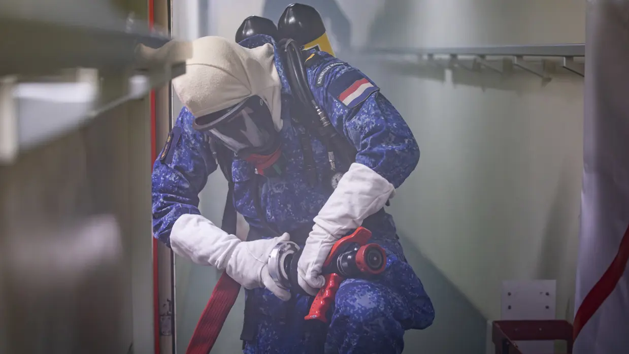 Een marineman draagt een persluchtmasker en in omgeven door rook aan boord.