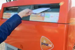 Iemand stopt een brief in een brievenbus.