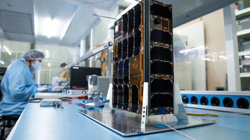 BRIK II satelliet in een productieruimte. Op de achtergrond een werknemer.