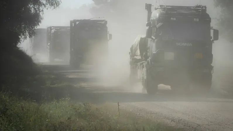 Militaire vrachtwagens rijden over een stoffig pad