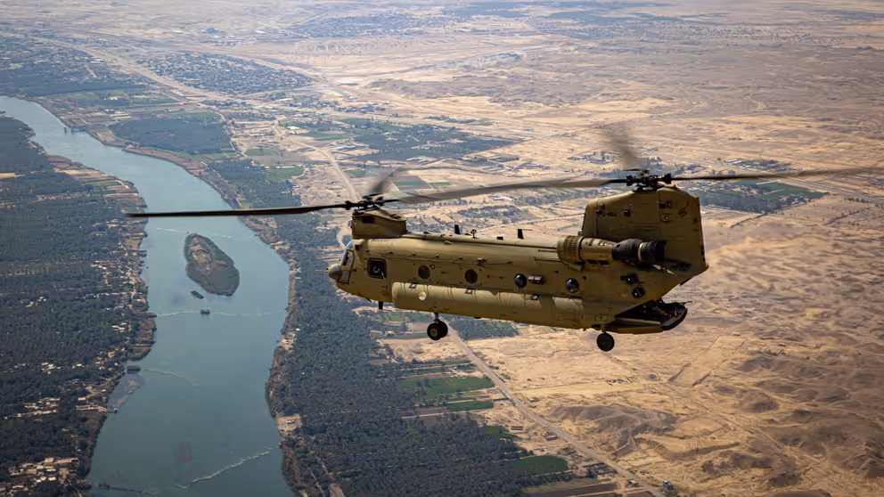 Chinook-transporthelikopter boven een meanderende rivier en woestijngebied.