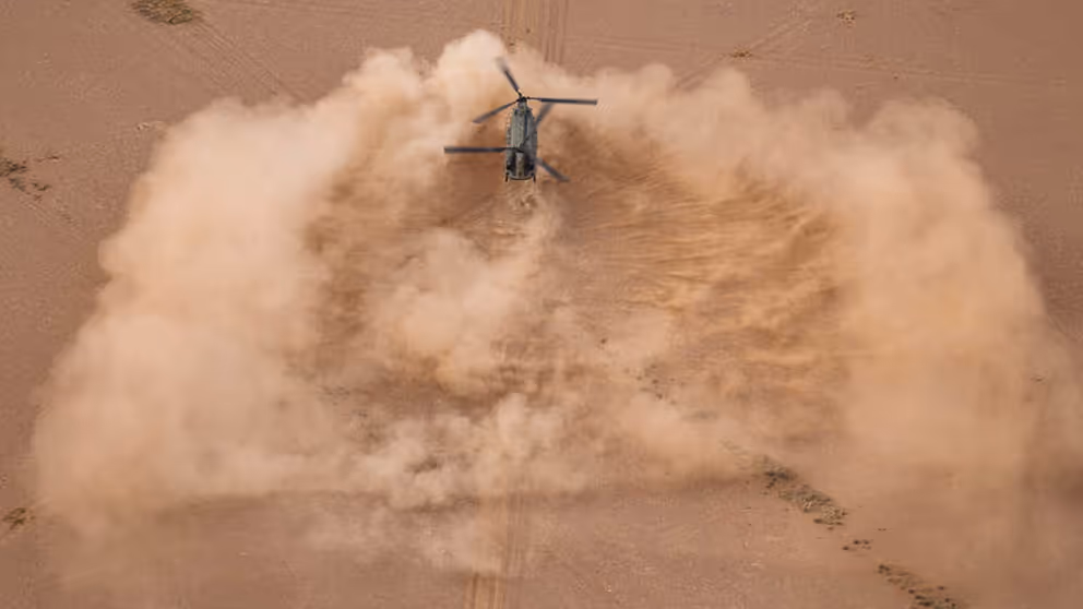 Chinook-transporthelikopter boven een enorme wolk opstuivend zand. Alleen maar bruin/oranjetinten.