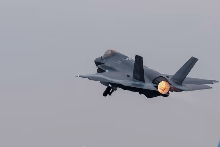 Een F-35 vliegt, terwijl daaronder reguliere vliegtuigen taxiën.