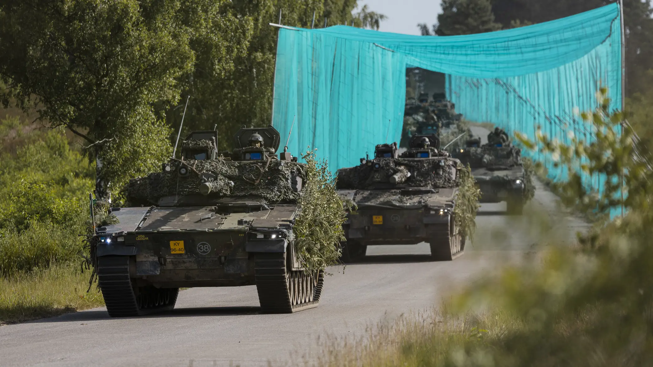 Militaire voertuigen rijden achter elkaar over de weg.