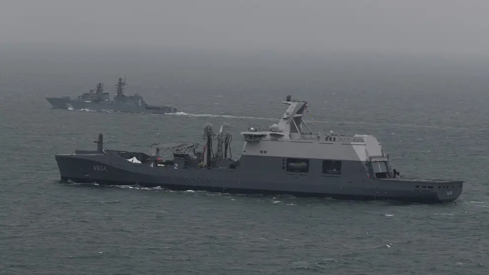 Een marineschip escorteert een ander schip op zee.