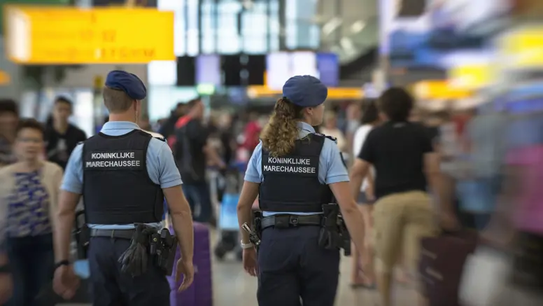 Twee marechaussees tussen het publiek op Schipol, op de rug gezien.