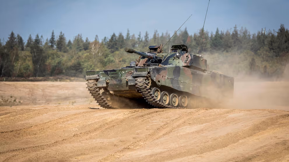 Een CV90 rijdt over een zandvlakte. 
