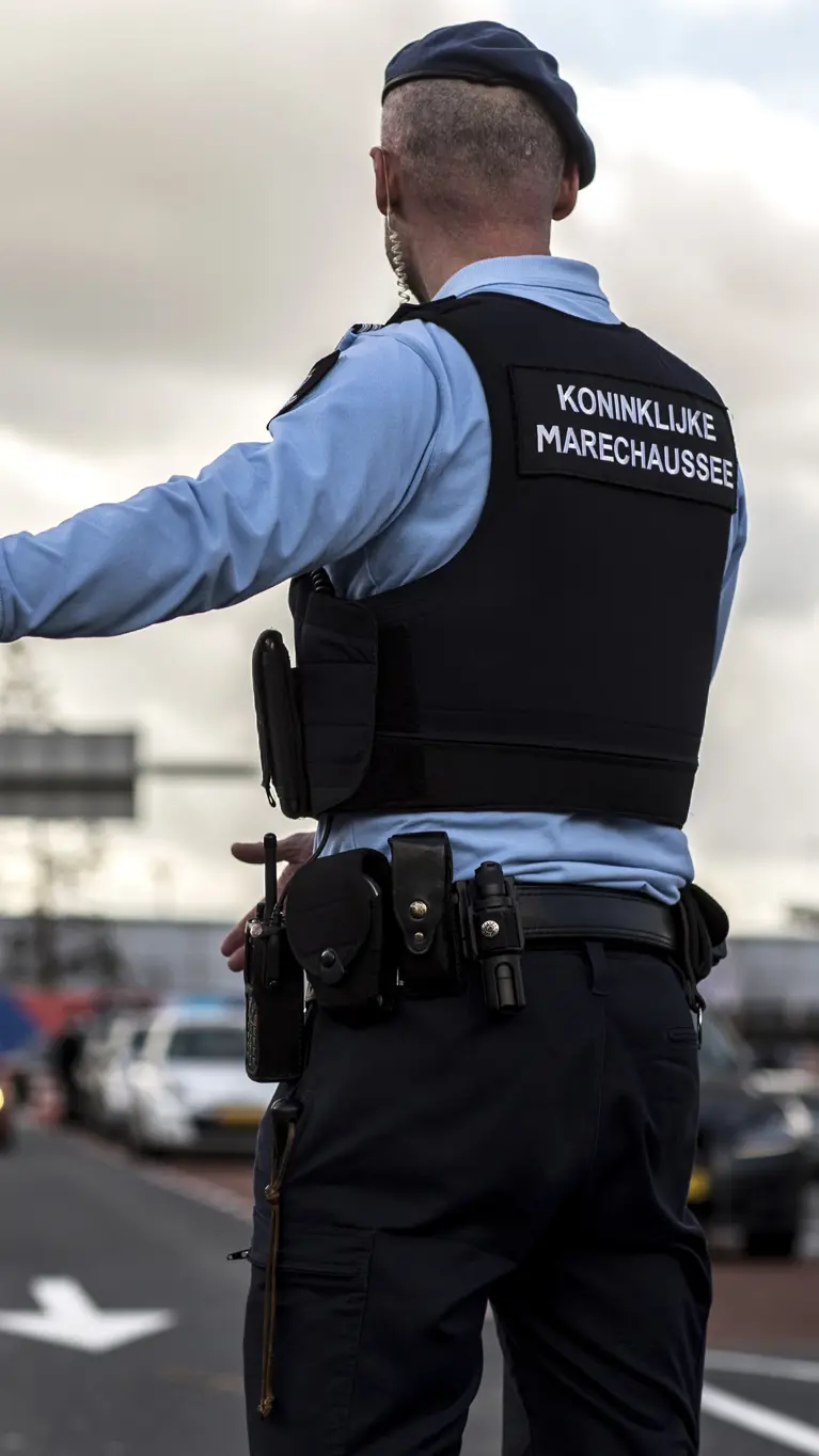 Een marechaussee op de rug gezien, wijst een voertuig naar de controleplaats.